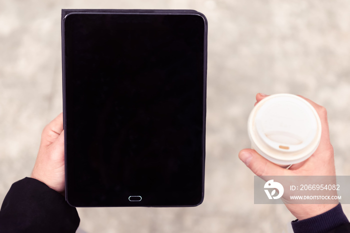 close up portrait of a business man holding a tablet device and carrying his coffee during a work meeting break. background up view image of a black kindle laptop. concept about tech, social, online