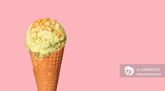 Pistachio or mint ice cream in cone on a pink pastel background. Knob, ball, scoop of ice cream decorated with golden and colorful sprinkles. Close-up of sweet dessert. Free copy space.