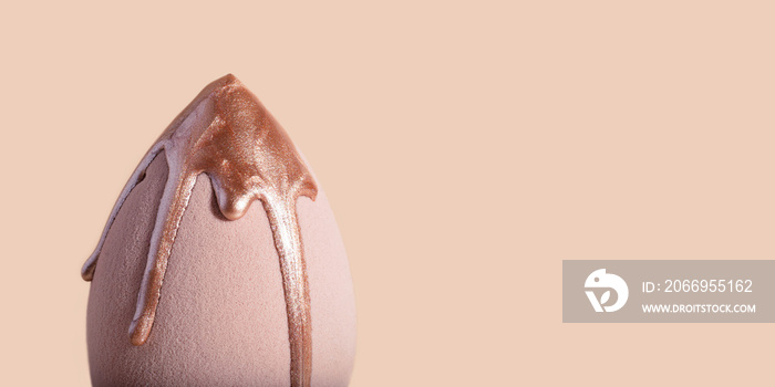 Closeup photography of beauty blender with dripping bronzer on it.Neutral beige background,large banner with copy space.