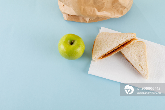 High angle view of green apple with peanut butter and jelly sandwich by paper bag on table