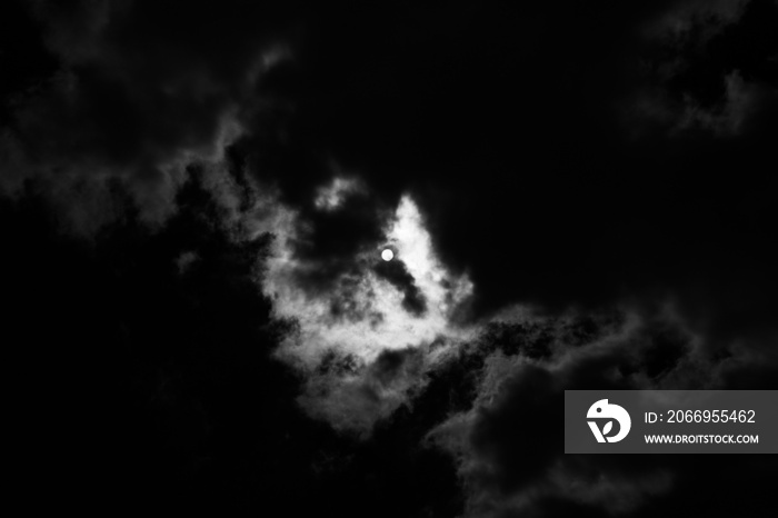 Black and white photo moon behind the clouds.