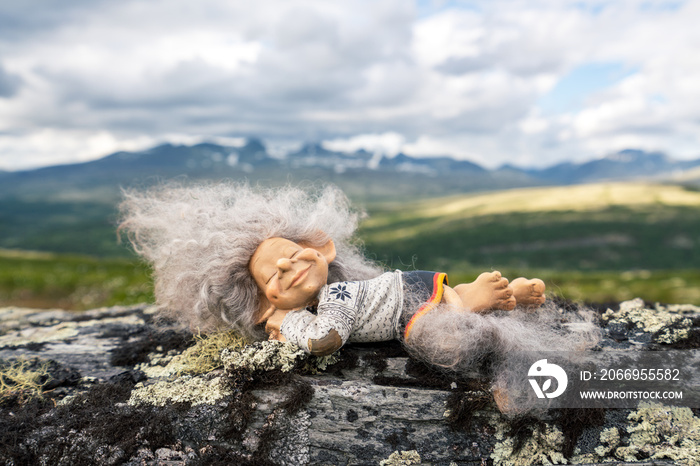 Beautiful peaceful and sleeping troll girl figure relaxing outdoors with mountain scenery in the background.