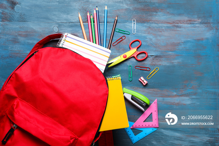 Composition with rucksack and school stationery on color wooden background, top view