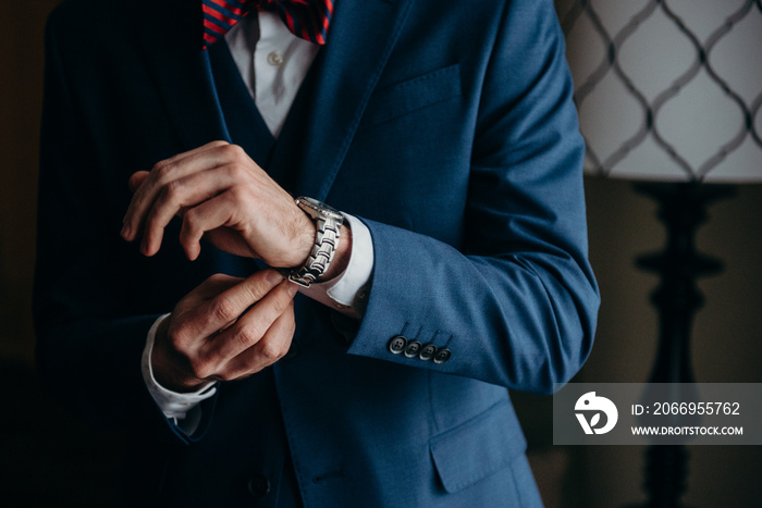 Groom adjusting his watch band in a blue suit with a red striped bow tie