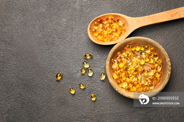 Bowl and spoon with fish oil capsules on grey background