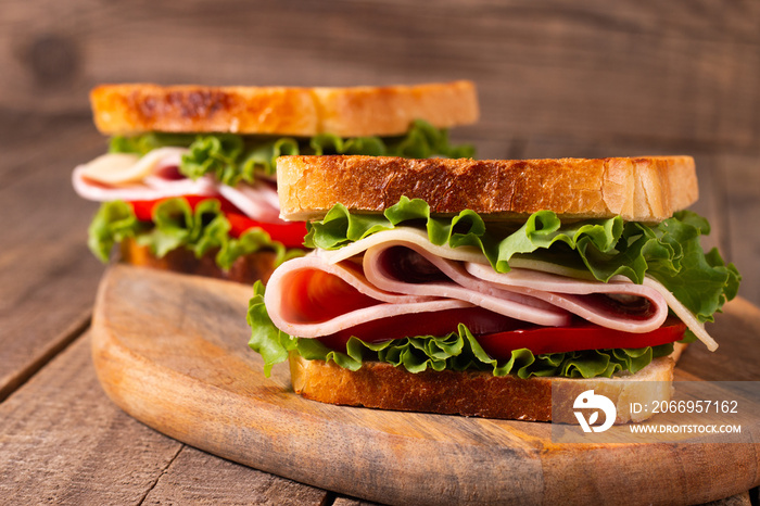 Close-up of two toasted sandwiches with fresh ham, cheese and vegetables on background. Club sandwich and take-away concept. Fast food.