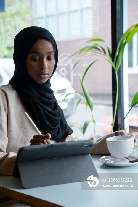 Young woman in hijab working on tablet in cafe