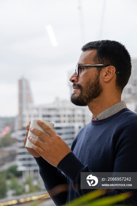 Man with coffee mug looking out window