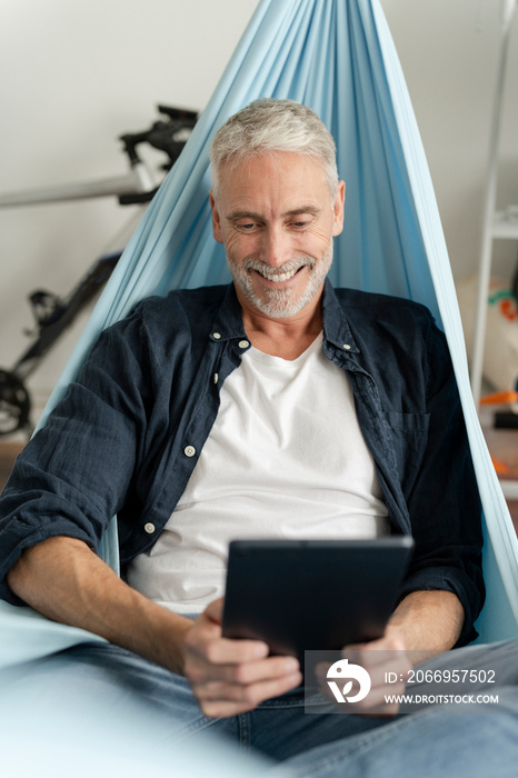 Smiling mature man using digital tablet in hammock