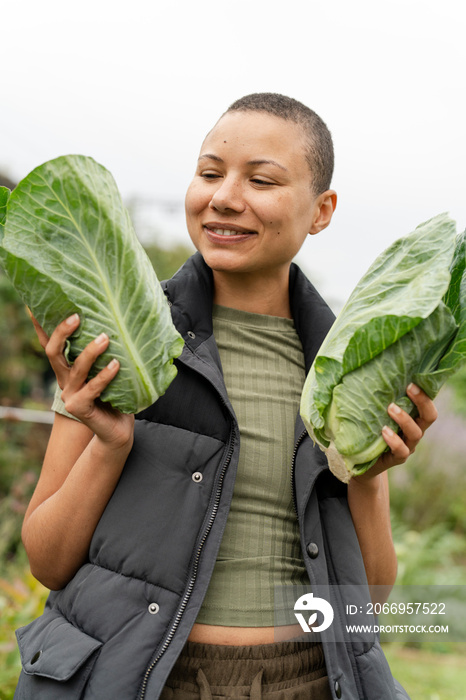 Portrait of smiling woman holding homegrown cabbages in urban garden