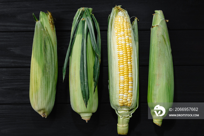 Cobs of ripe raw corn laid out on a table with a dark wooden texture. Healthy summer food concept. Fresh unroasted cob of corn. Background, top view, close-up, flat plan, copy space.