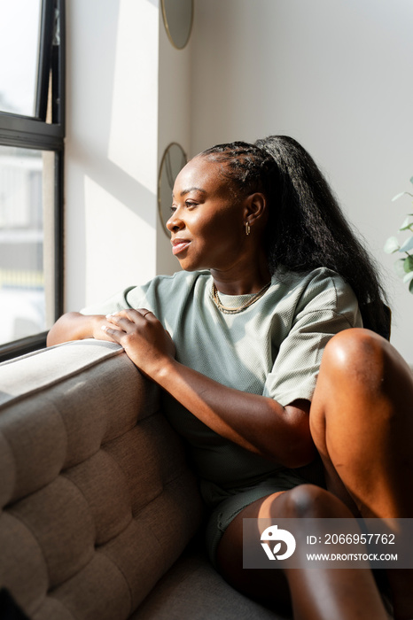 Portrait of young woman looking through window at home