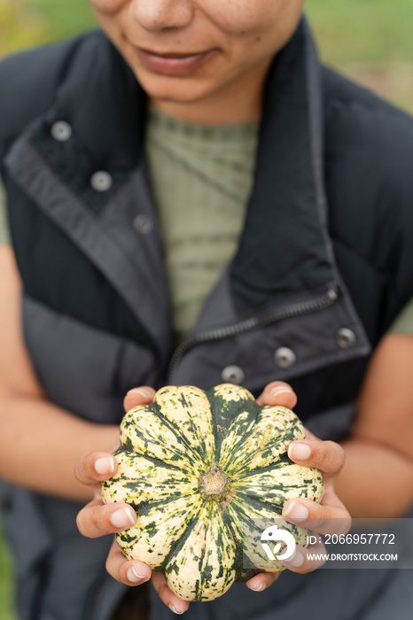 Mid section of woman holding homegrown gourd in urban garden