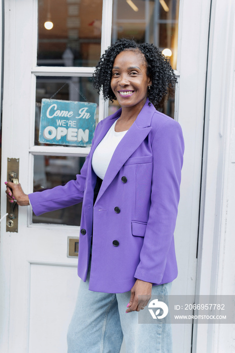 Smiling woman in purple jacket standing in front of open store