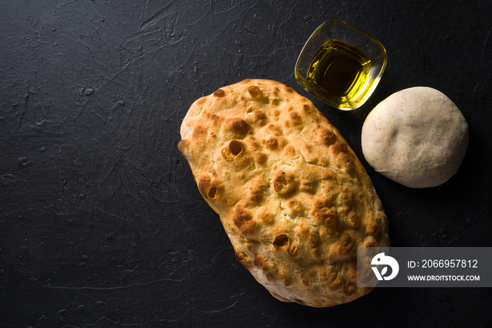 Roman focaccia with ingredients and dough for preparation on dark background