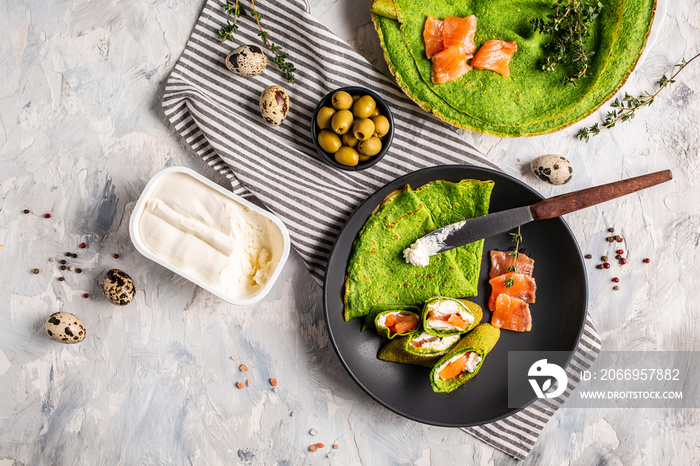 spinach crepes or pancakes with smoked salmon and cream cheese. Delicious breakfast or snack on a light background, Trendy vegetarian food. top view