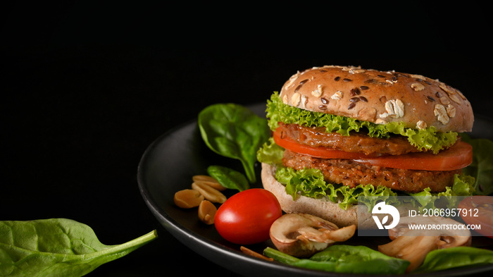 Plant based burger with fresh and organic vegetables on a plate in black background.