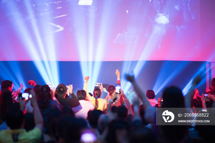 Rear view of crowd with arms outstretched at concert or seminar training in hall