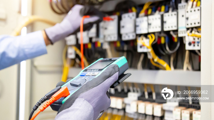 Electrical engineer using digital multi-meter measuring equipment to checking electric current voltage at circuit breaker and cable wiring system in main power distribution board.