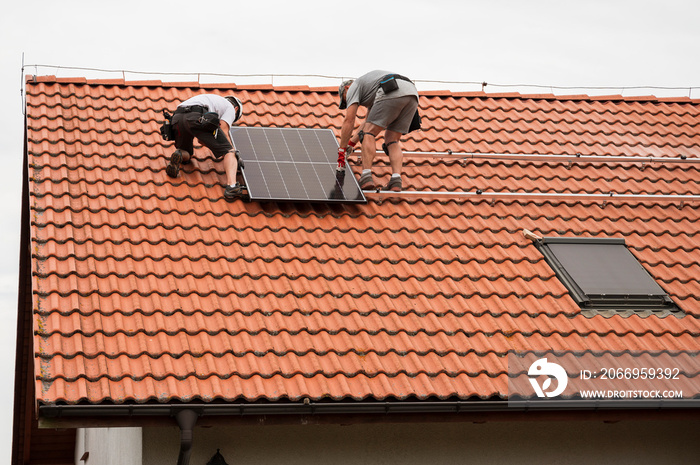 Two engineers on the house roof assemble photovoltaic panel.