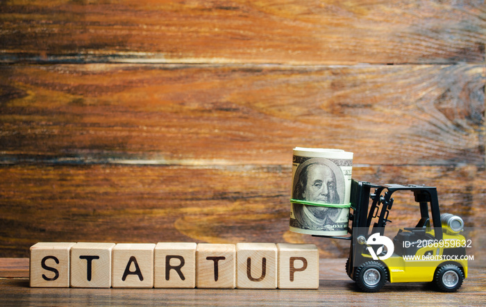 Forklift truck carries a bundle of dollars to inscription Startup. The concept of raising funds for a startup. Crowdfunding. Raising funds and resources to complete a commercial or intangible project.