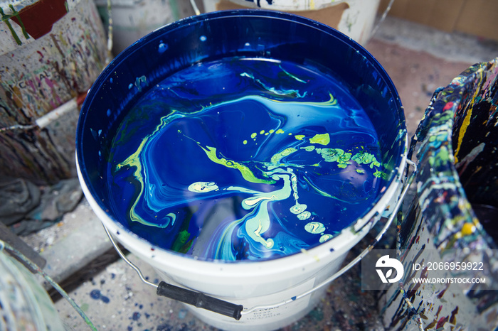 A vibrant large pot of blue, aqua and greens mixed acrylic block printing and screen printing paint in a bucket in an industrial creative art studio setting.