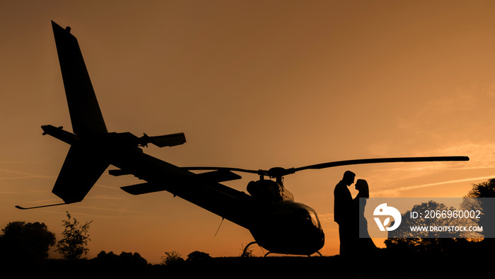 Bride and groom wedding day sunset silhouette with a Helicopter against an orange sky.