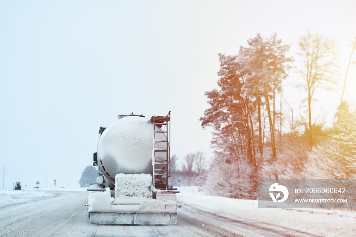 Truck with cargo tank on slippery snow winter road outside the city, back view