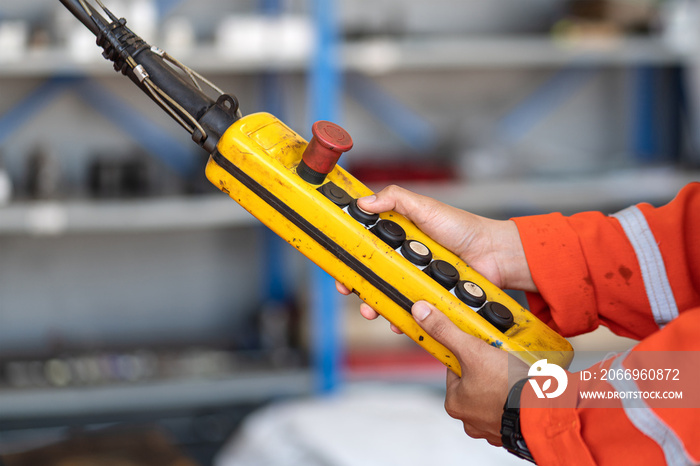 A worker is operating remote swtich to control overhead crane at the factory warehouse. Industrial working action photo. Close-up.