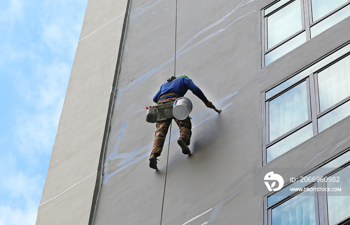 Climber worker hanging on ropes to repair building service on high rise building.