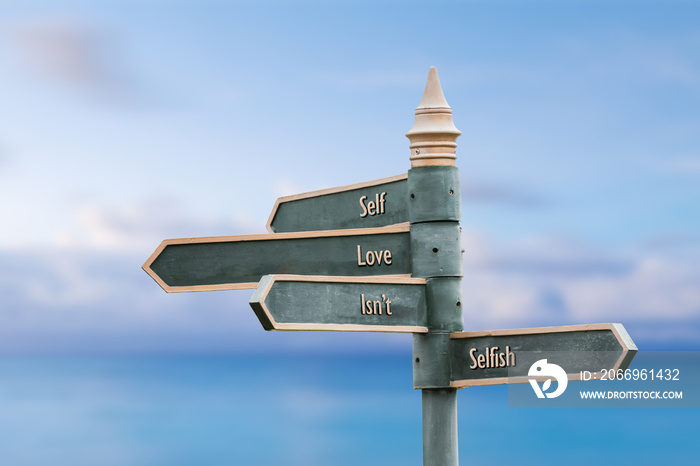 self love isnt selfish four word quote written on fancy steel signpost outdoors by the sea. Soft Blue ocean bokeh background.