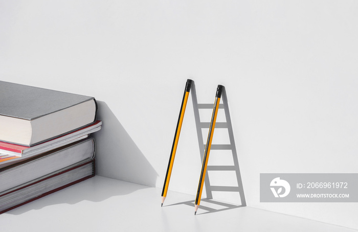 Two pencils and shadow in form of ladder with stack of textbooks on white tabletop, Education, learning is the ladder to success concept