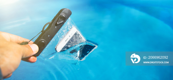 Waterproof phone case. Immerse the phone in water. Shooting underwater. protection from moisture. The hand lowers the phone in the case into the water.