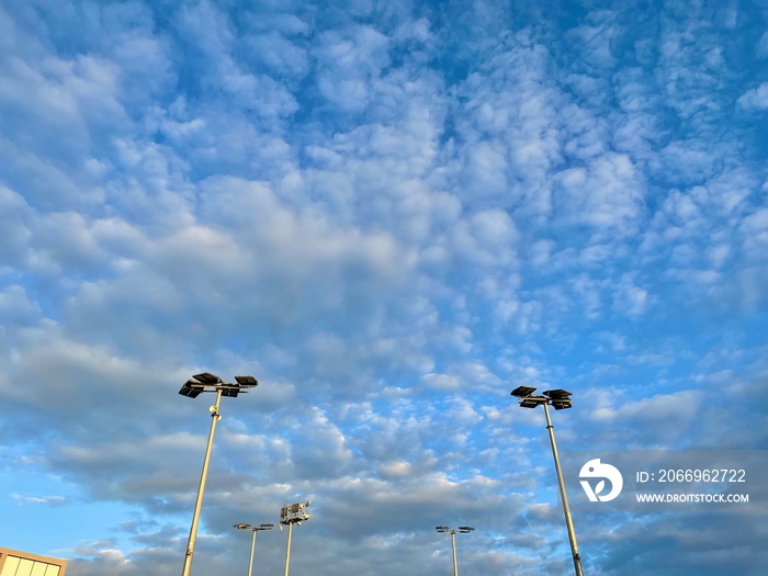 Lights posts at tennis courts agains blue sky and clouds