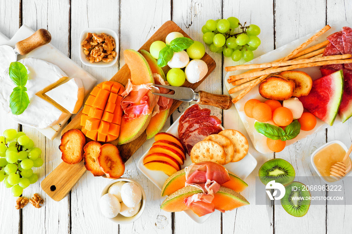 Summer fruit theme charcuterie table scene against a white wood background. Collection of fruits, cheese and meat appetizers. Above view.