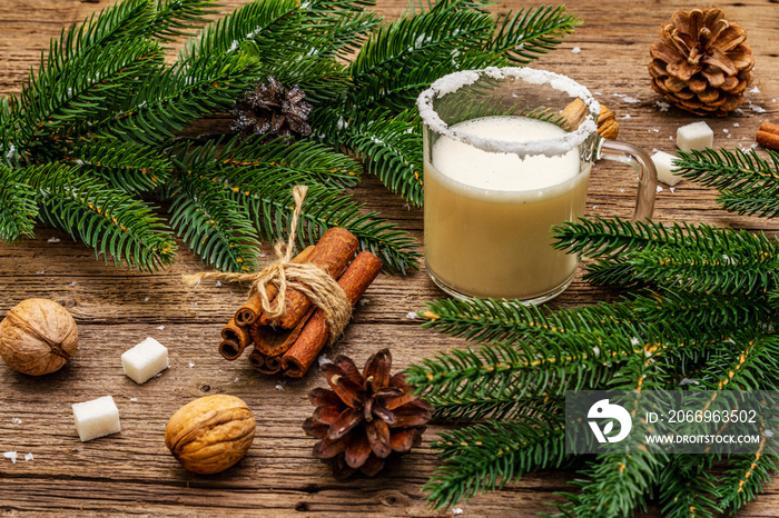 Christmas eggnog liqueur or cola de mono cocktail. Classical winter drink in glass mug, xmas decorations. Evergreen branches, cinnamon, walnuts, sugar. Old wooden background