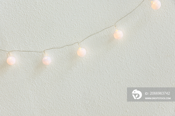 Christmas New Year Background. Diagonal Hanging Pastel Golden Cotton Balls Garland White Wall Background. Scandinavian Style. Glittering Lights. Cozy Festive Atmosphere. Poster with Copy Space