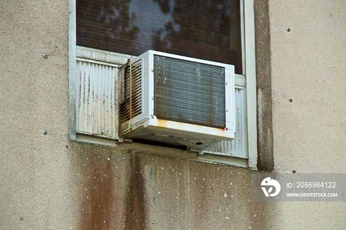 An old white, moldy and rusted window mounted air conditioner on cement wall, showing drips