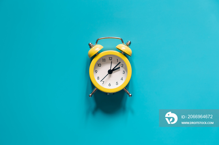 Yellow alarm clock on blue background isolated, flat lay.