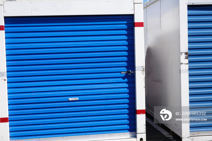 A white storage pod container with a blue door on a asphalt road in front of some stores