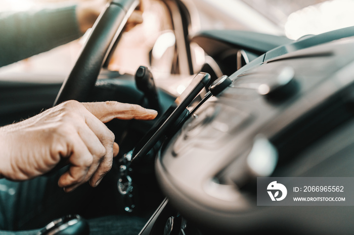 Close up of Caucasian senior man turning on navigation on smart phone while sitting in his car.