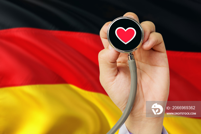 Doctor holding stethoscope with red love heart. National Germany flag background. Healthcare system concept, medical theme.