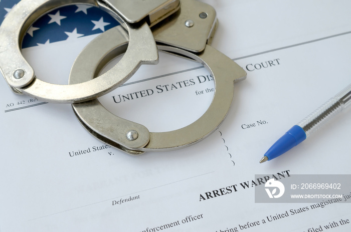 District Court Arrest Warrant court papers with handcuffs and blue pen on United States flag. Concept of permission to arrest suspect