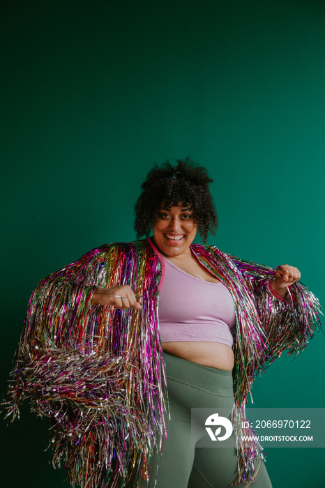 portrait of a plus size person dancing with a rainbow tinsel jacket