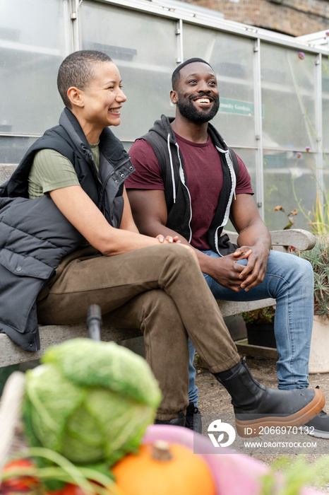 Smiling couple relaxing on bench in front of greenhouse