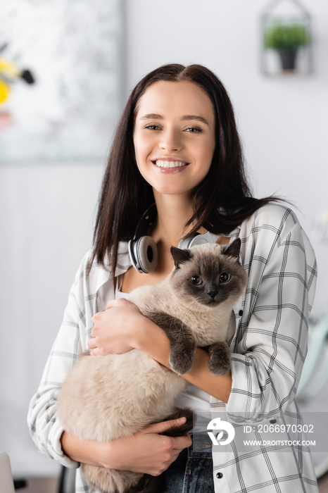 happy young woman looking at camera while holding cat at home