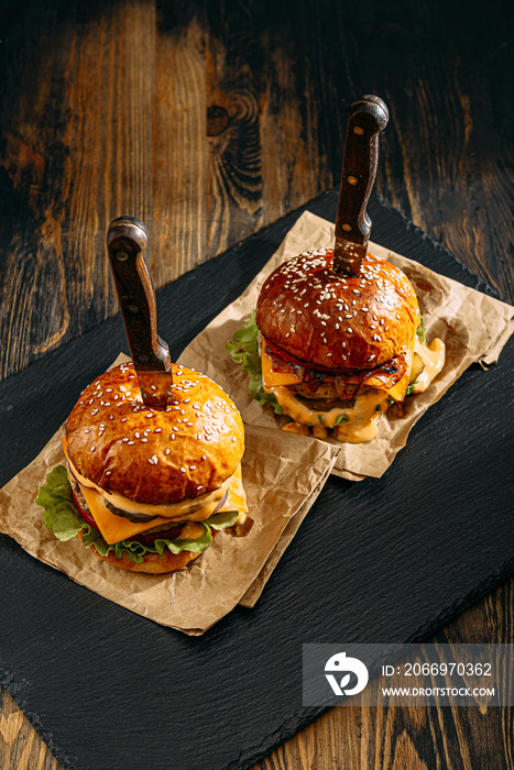 Two mouth-watering, delicious homemade burger used to chop beef. on the wooden table. The burgers are inserted knives.