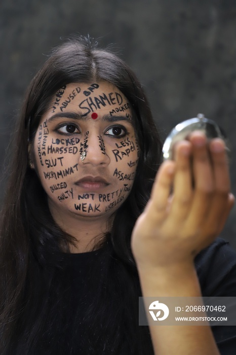 A southeast Asian brown young woman protesting gender based violence by writing anti violence against women and girls messages all over her face