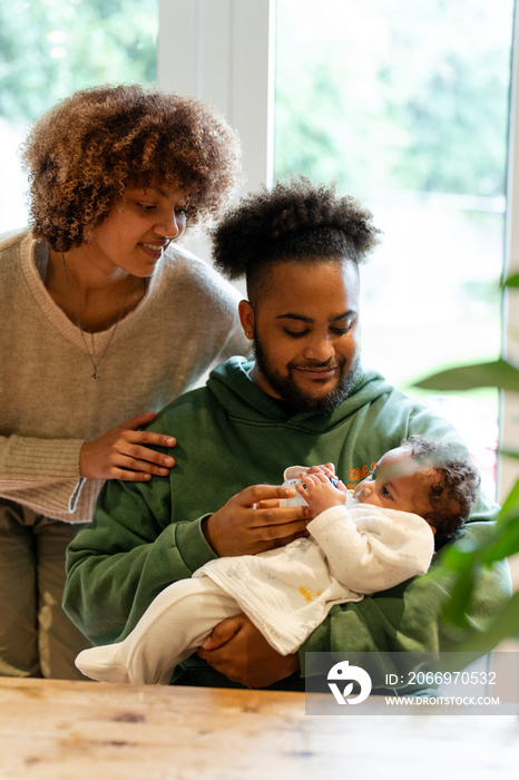 Mother looking at father feeding baby daughter at home