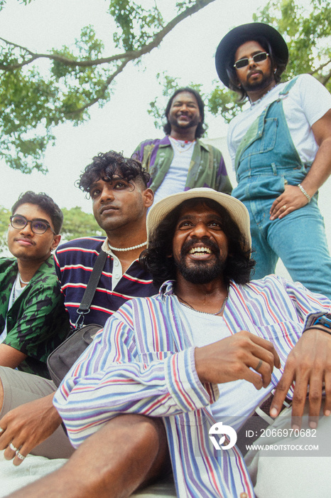 Malaysian Indian men in a group against a cloth backdrop in a park surrounded by trees, talking, laughing and sitting together